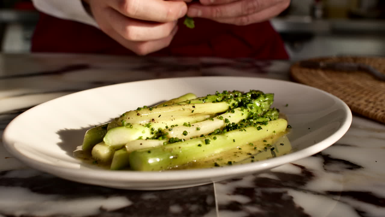 chef's hand sprinkling seasoning over a plate of fresh green and white asparagus in a generic kitchen. Professional culinary finishing touch and food styling