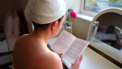 Mujer-Relajada-Leyendo-Un-Libro-Después-De-La-Ducha-Con-Toallas-Puestas,-Sentada-En-La-Ventana-Después-Del-Baño