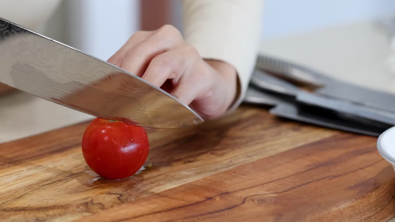 A woman slices a tomato on a wooden cutting board in a well-lit kitchen, emphasizing precision and culinary skill