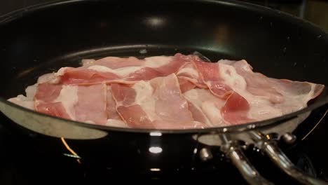 vista de cerca: el tocino en la sartén se encoge y se enrosca a medida que se cocina