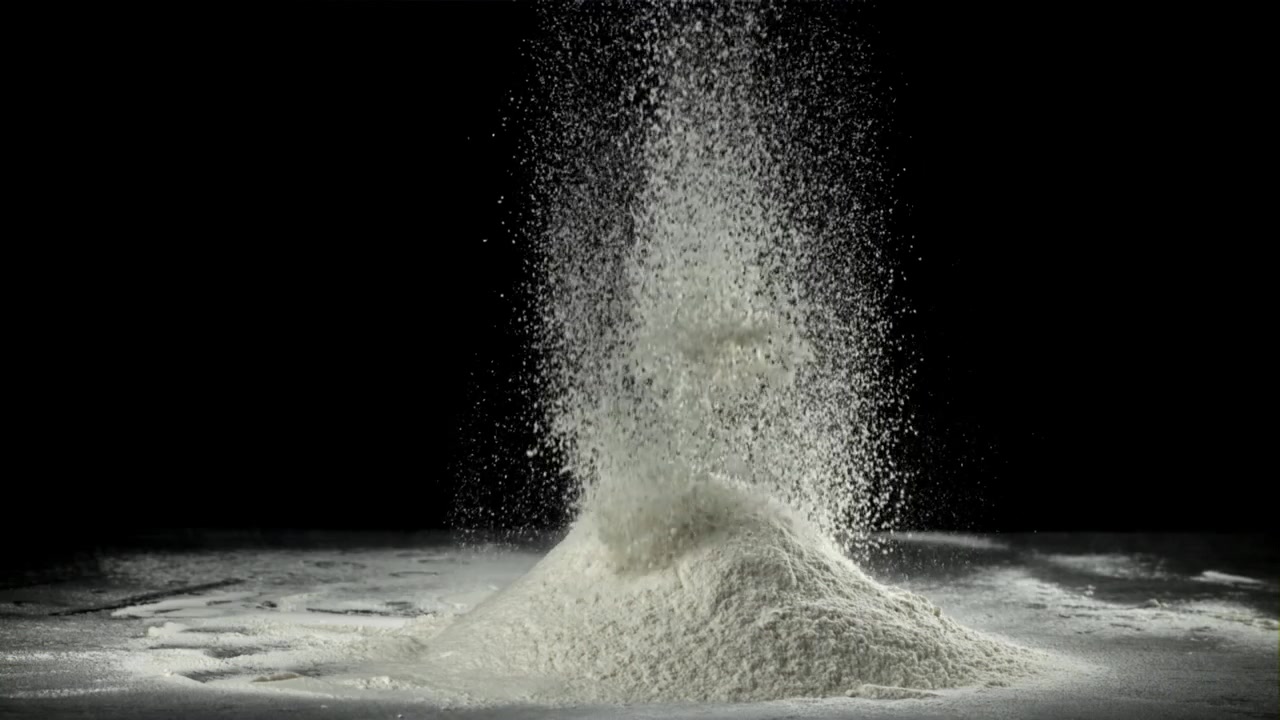 Hvidt pulver falder og samler sig på en mørk overflade i slowmotion