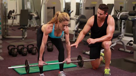 mujer levantando una barra con su entrenador en una sesión de crossfit