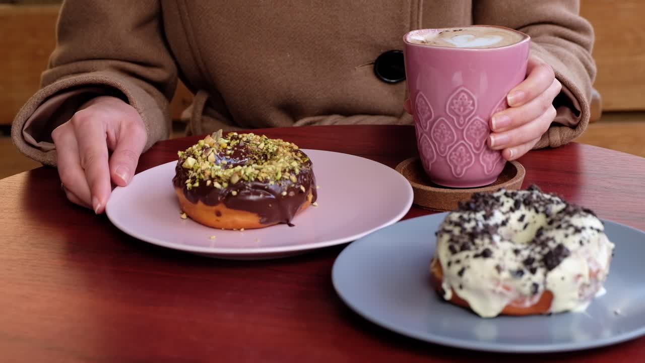 Close up of a woman in a brown coat eating donuts and drinking coffee at a cafe