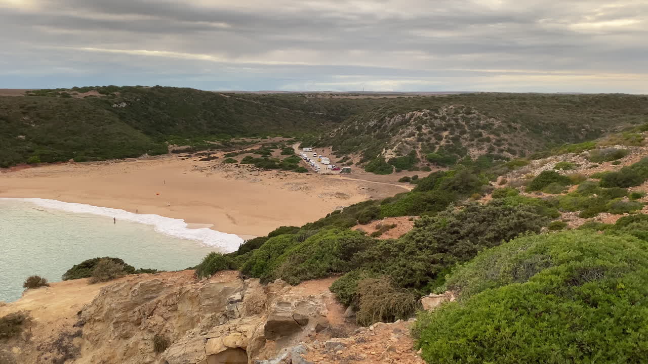 Dalla cima della scogliera, il vasto Atlantico si estende oltre le dune e le sabbie dorate di Sagres. I pendii aridi di Sagres si ergono sotto un cielo nuvoloso, rivelando le trame e i colori della costa atlantica.