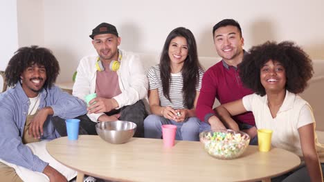 diverse group of friends smiling while relaxing on a couch with snacks