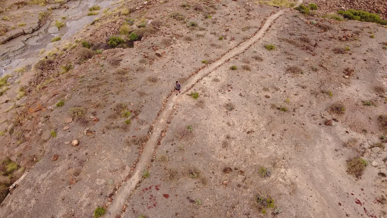 Bird's eye view of solo man walking on hiking trail next to dry river bed of tenerife