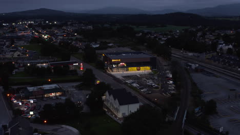 Aerial-footage-of-glowing-building-at-road-in-evening-town.-Modern-cinema-with-car-park.-Killarney,-Ireland