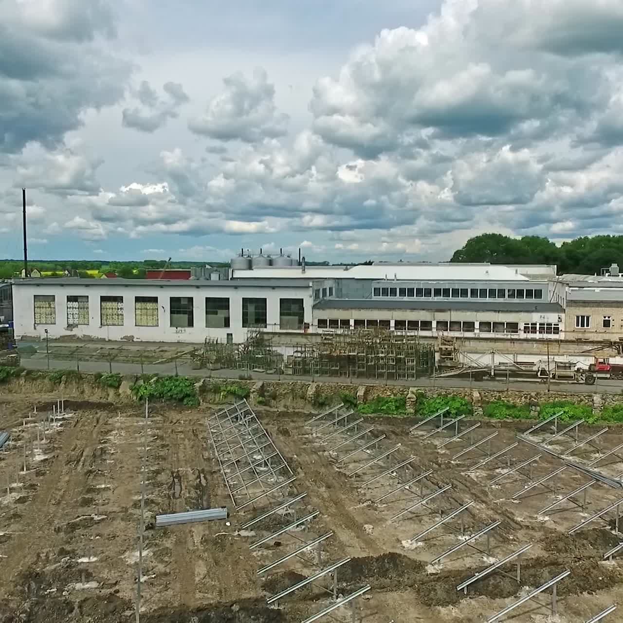 Construction site with workers working on. Metal supports prepared on the ground for installing solar panels. Industrial warehouses at backdrop