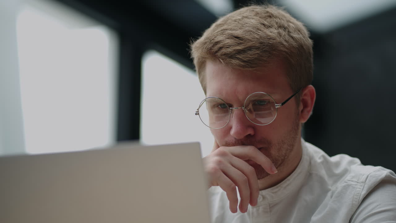 Portrait of a tired pensive man looking at a laptop screen with glasses. A man brainstorms. Problem solving. Think and work