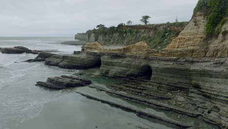 vuelo aéreo sobre la parte superior del paisaje costero escarpado y escarpado y cuevas en los acantilados de omau, cabo de viento en la isla sur de nueva zelanda aotearoa