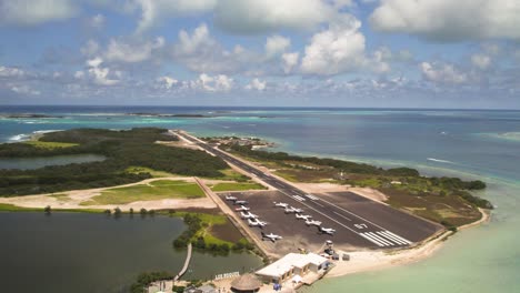 Gran-roque-los-roques-airstrip-with-parked-planes-and-turquoise-waters,-sunny-day,-drone-shot,-aerial-view