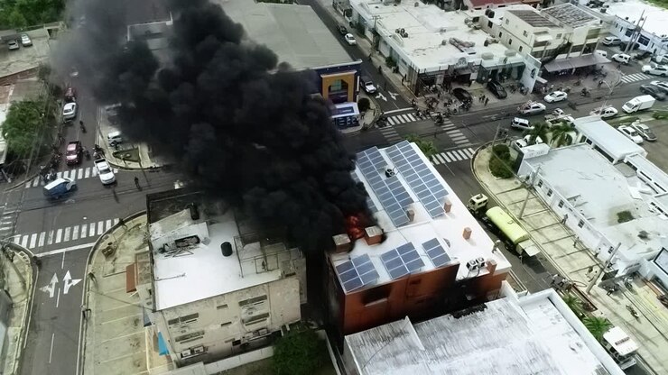 Vista aérea de un edificio en llamas, debido a una explosión, con humo oscuro elevándose, en Haití - vista estática, vista de dron
