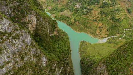 Slow-downward-reveal-of-gorgeous-turquoise-green-water-cutting-between-two-steep-mountains