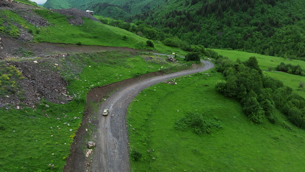 coche conduciendo por un camino de tierra en una ladera cerca de la aldea de ushguli en georgia - toma aérea