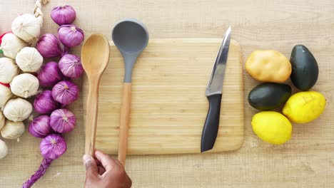 a hand holds a wooden spoon on a cutting board with ingredients for a meal