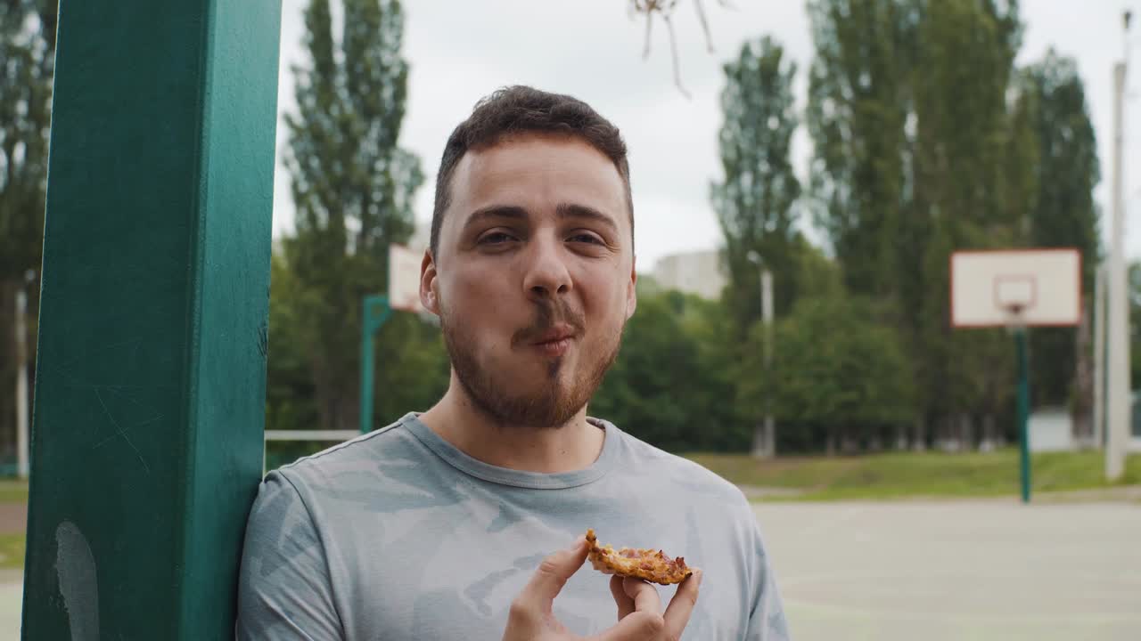 un hombre guapo comiendo pizza en una cancha de baloncesto