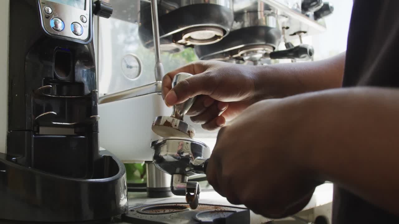 Close up of african american male barista making coffee using coffe machine at cafe