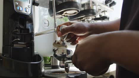 close up of african american male barista making coffee using coffe machine at cafe