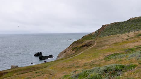 Tiro-De-Acantilado-Junto-Al-Mar,-Sendero-A-Lo-Largo-Del-Mar-En-Calma,-Día-Gris,-Hierba-Verde