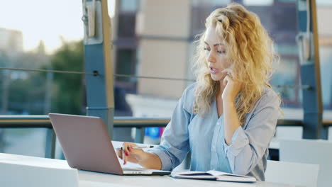 Attraktive-Geschäftsfrau,-Die-Telefoniert,-Sitzt-In-Einem-Café-Auf-Der-Terrasse-und-Arbeitet-Mit-Einem-Laptop