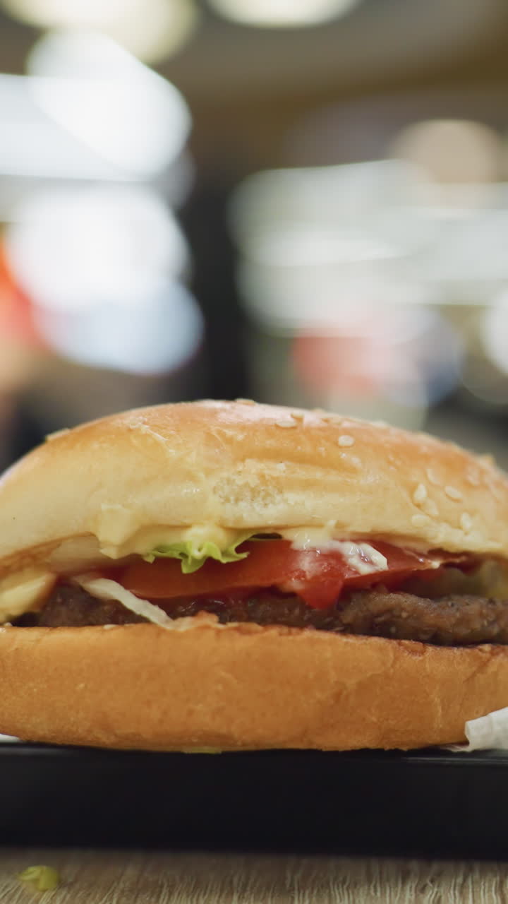 primer plano de papas fritas doradas y una hamburguesa en una bandeja negra en una mesa con un fondo borroso., destacando la deliciosa comida rápida en un entorno de comedor casual