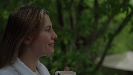a woman drinking coffee with a blurred green outdoor background
