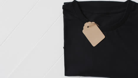 Video-of-flat-lay-of-black-t-shirt-with-tag-and-copy-space-on-white-background