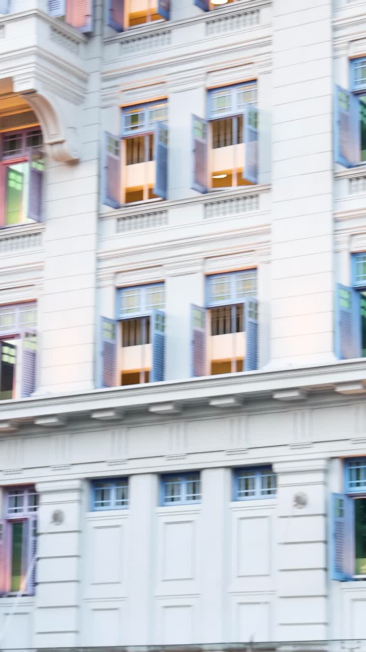 La telecamera panoramica su un palazzo storico a più piani con persiane colorate, luce diurna soffusa e alberi rigogliosi visibili.