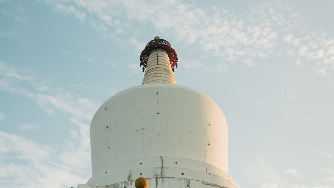 Maestosa stupa nella luce del mattino. Scena pacifica con corona dorata e nuvole sparse. Paesaggio calmo che cattura una stupa bianca adornata con una corona dorata sotto un cielo blu chiaro con nuvole leggere.