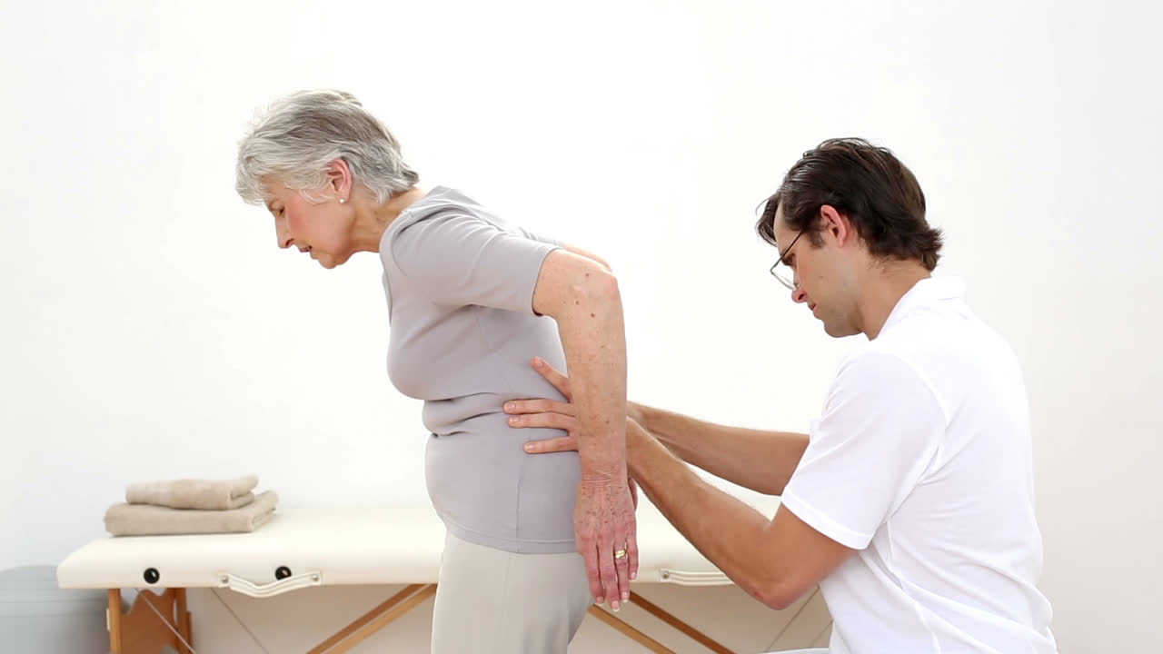 fisioterapeuta revisando la parte inferior de la espalda de los pacientes de edad avanzada