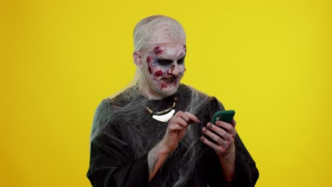 Frightening-man-Halloween-zombie-using-mobile-phone-typing-new-post-on-web,-browsing,-addiction