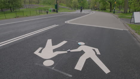 static wide shot with bike approaching and painted pedestrian symbols on road surface with surgical mask and hand sanitizer, central park, new york city
