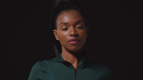 Portrait-Of-Determined-Female-Athlete-Wearing-Tracksuit-Training-And-Preparing-Psychologically-For-Sports-Event-Against-Black-Studio-Background