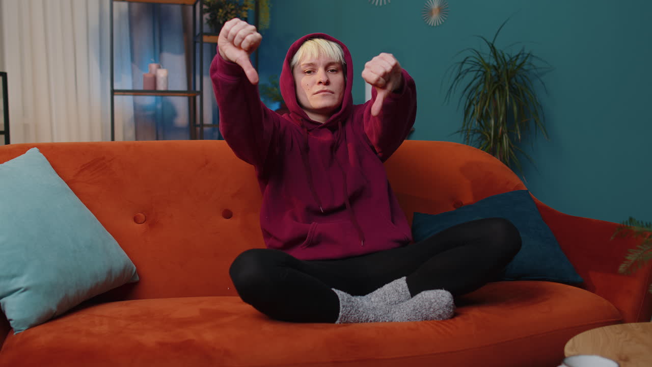 Upset young woman showing thumbs down, dislike bad work, disapproval, dissatisfied feedback at home