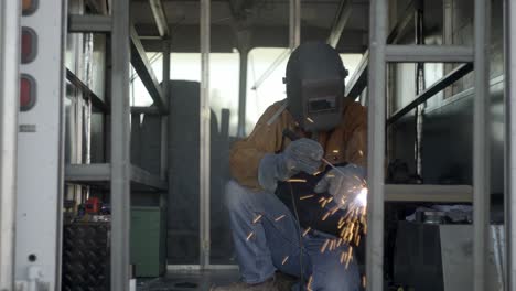 man welding metal framework in delivery truck, then checks on weld