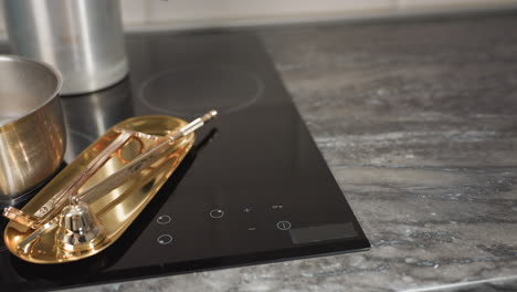 gas cooker with stainless pot and golden baking tray on black glass surface as kitchen towel is dropped beside tray, capturing moment of food preparation and cleanup in modern cozy kitchen setup