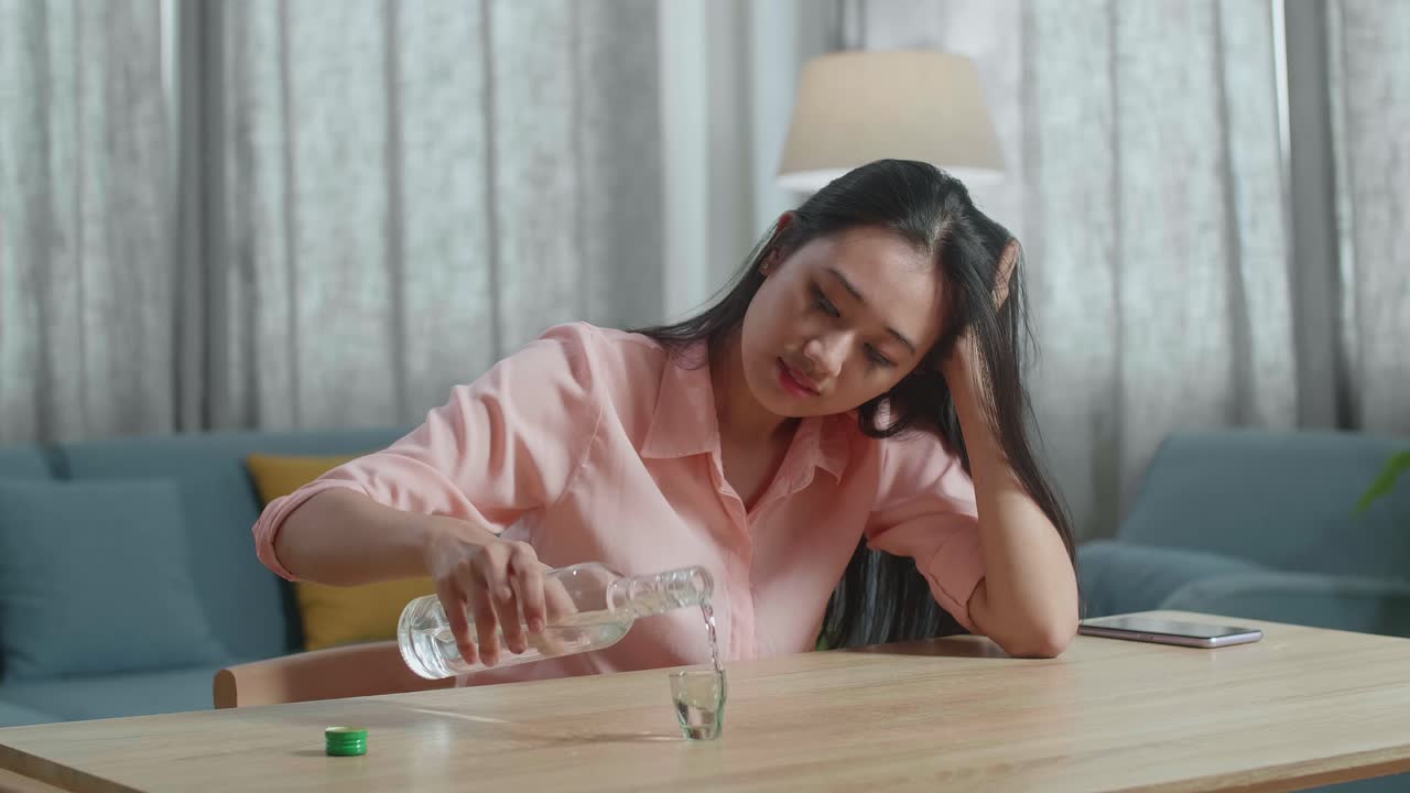 술에 취한 우울한 아시아 여성이 집에서 술을 마시기 전에 글라스에 보드카를 부어