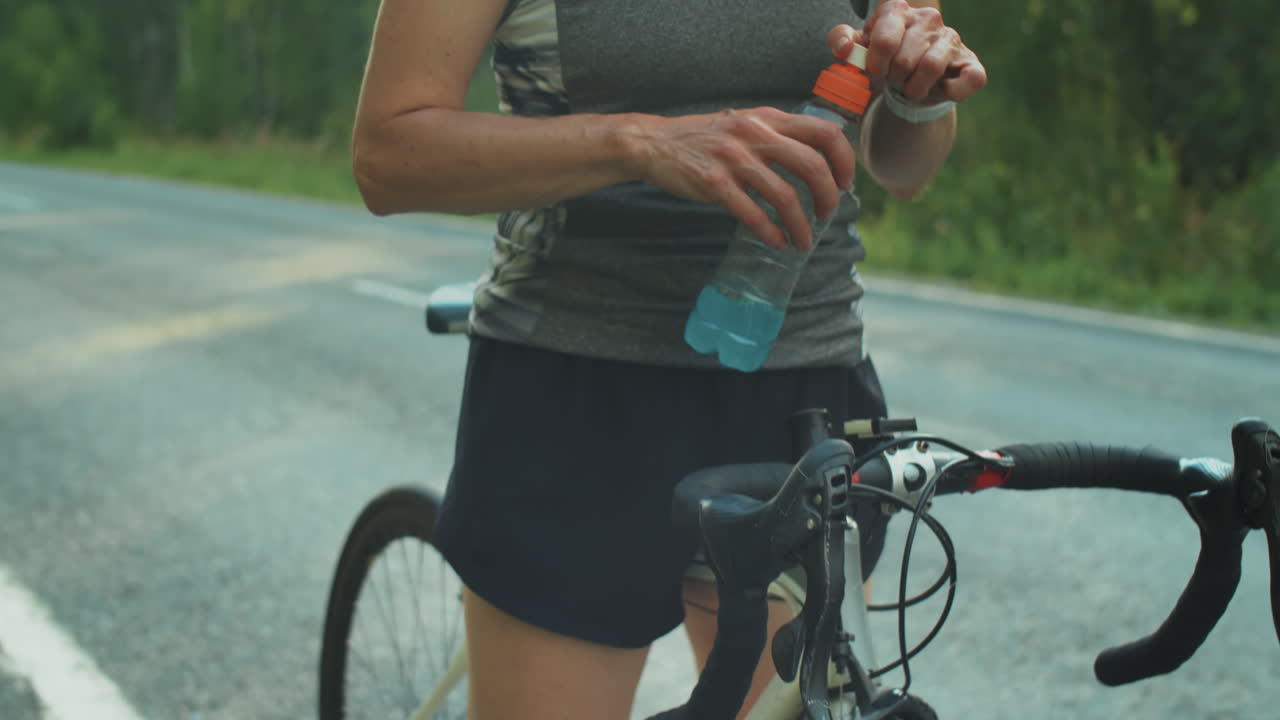 Atleta donna in piedi con la bici che beve una bevanda sportiva