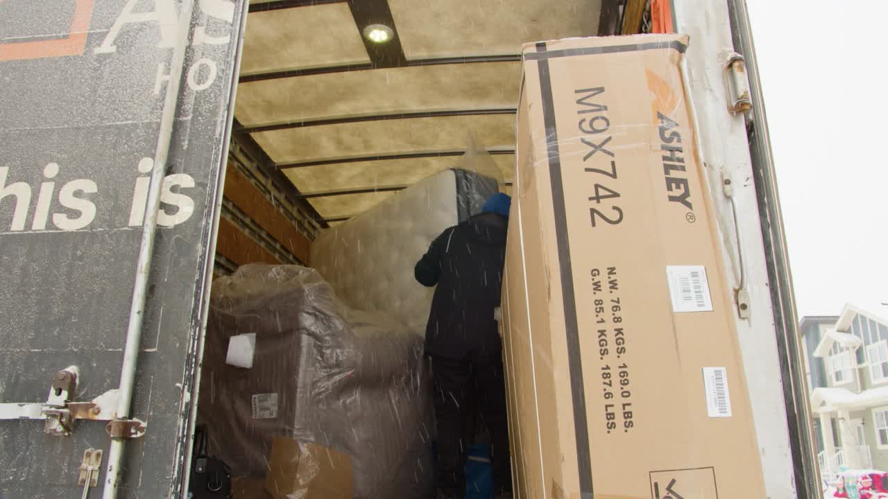 Static shot of delivery person inside truck pulling furniture box to the edge snowy winter neighborhood