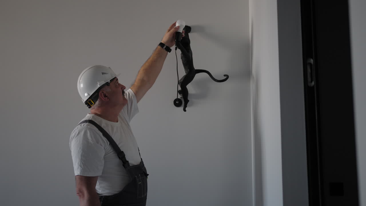 The electrician inserts and checks the operation of the light bulb in the lamp. Decorative Lamp Monkey