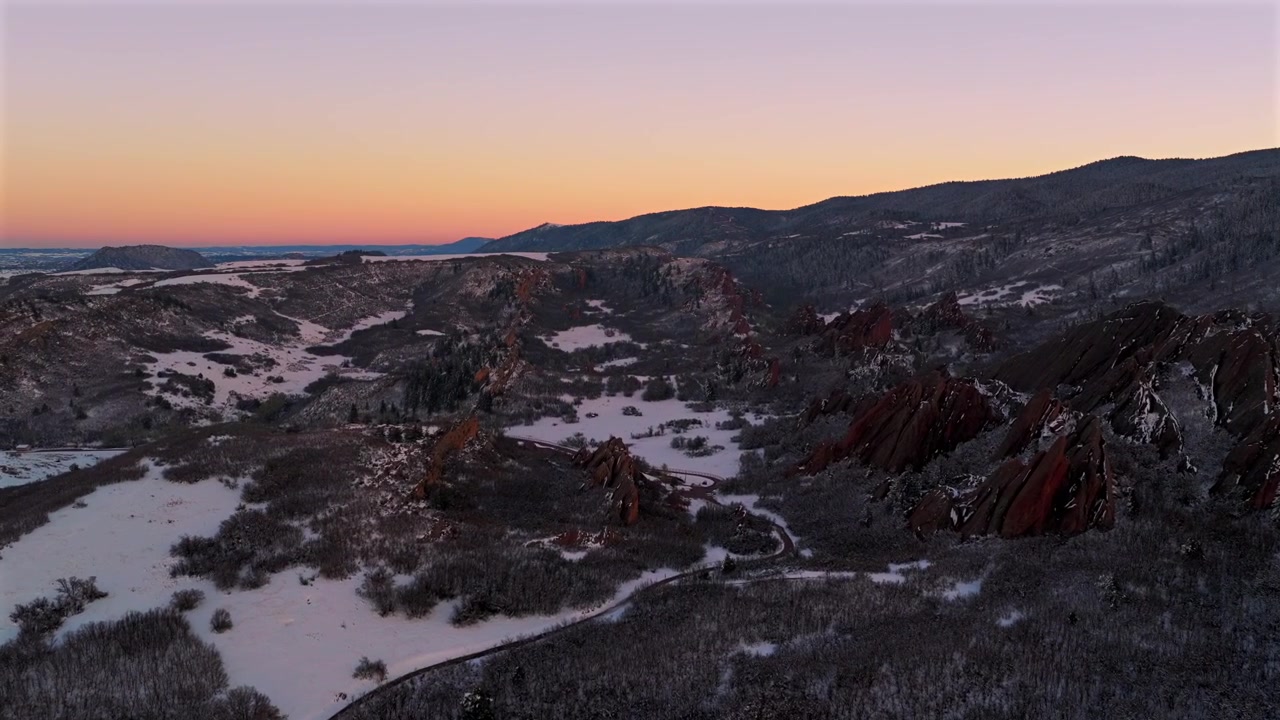 Pemandangan udara drone saat matahari terbenam di Taman Negara Bagian Roxborough, Jalur Lembah Fountain, dengan tengara batu pasir bergerigi Red Rocks yang tertutup salju, Sterling Ranch Colorado. Terlihat Lapangan Golf Arrowhead Littleton Denver Front Range, bergerak maju ke kiri