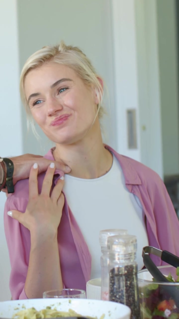 Vertical video: Tasting woman in pink top testing with spoon at table, smiling at shoulder touch