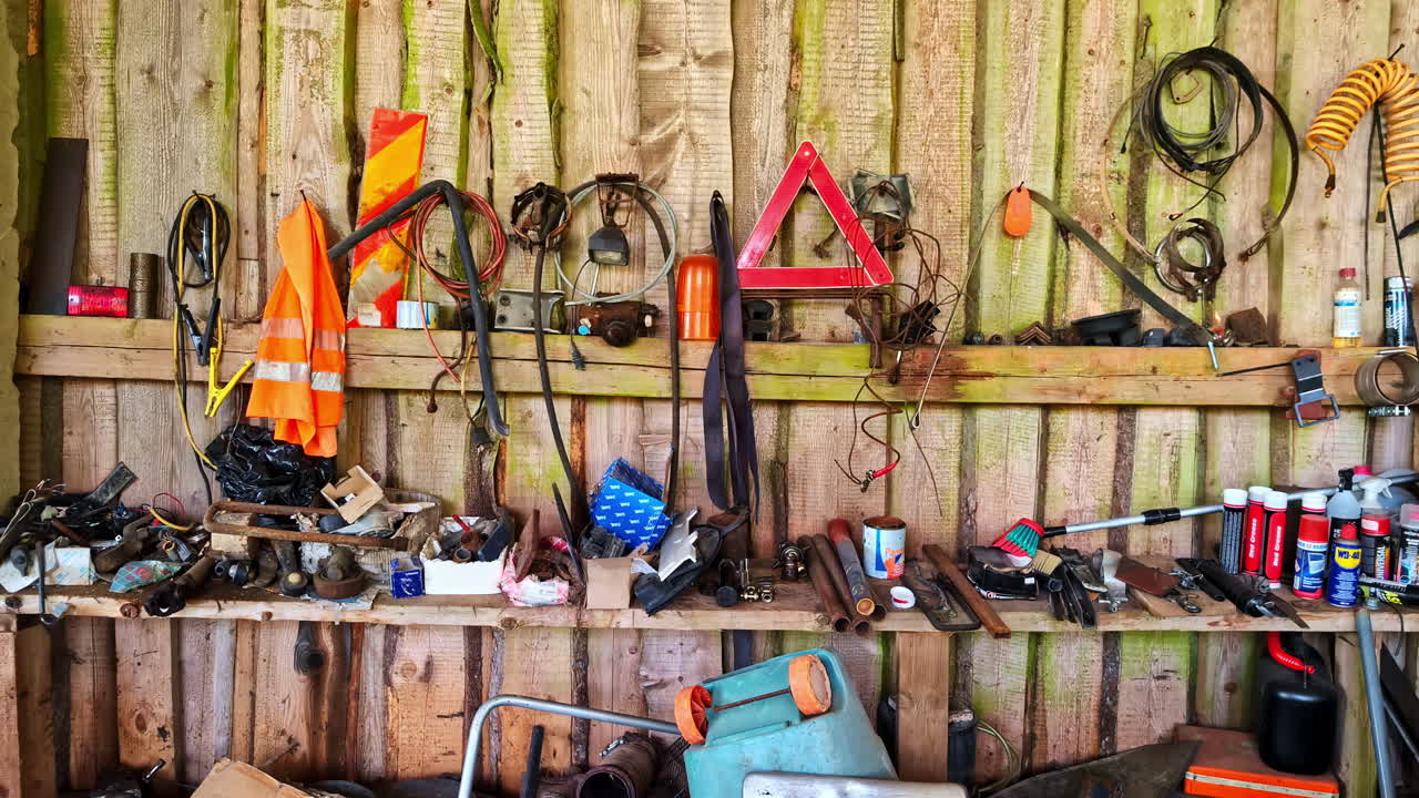 Slow push into shed with rustic hanging farm tools covered in rust and wear