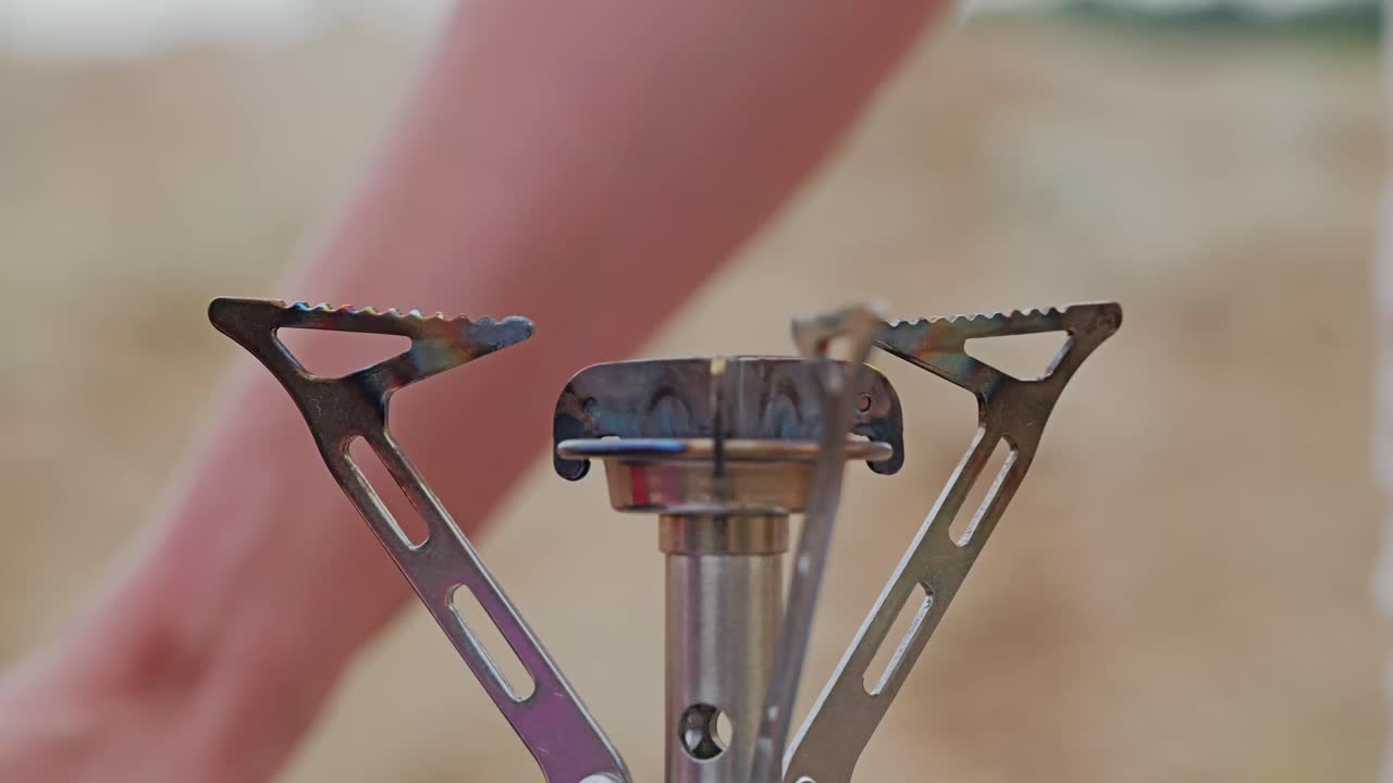 Detailed close up shows camping stove as woman places pan during outdoor cook