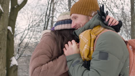 husband and wife in winter clothes warm their hands with their mouths in a snowy forest