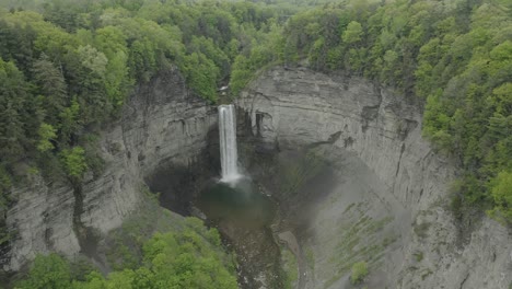 drone shot, flying to the left, showing a big waterfall, in a canyon with trees surrounding it