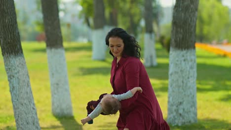happy mother shakes and circles the baby in her arms, cheerful childhood. mom plays with the child in the park, holds him in her arms. 4k, 10bit, prores