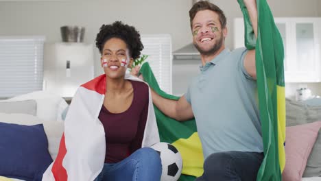 video de una feliz pareja diversa sosteniendo banderas de portugal e inglaterra y viendo el partido en la televisión