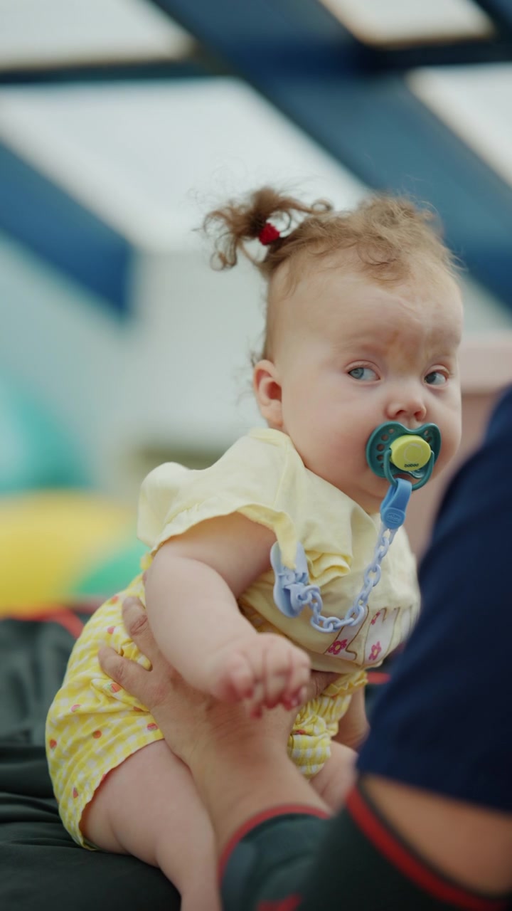 Infant girl with curly hair and a pacifier, held gently by a healthcare worker, highlighting pediatric care and support