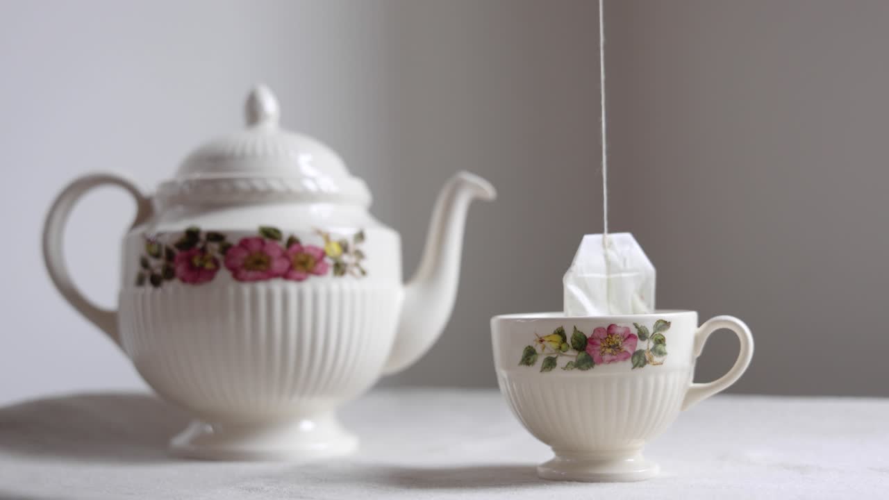 Bustina di tè immersa in una tazza da tè floreale con teiera.